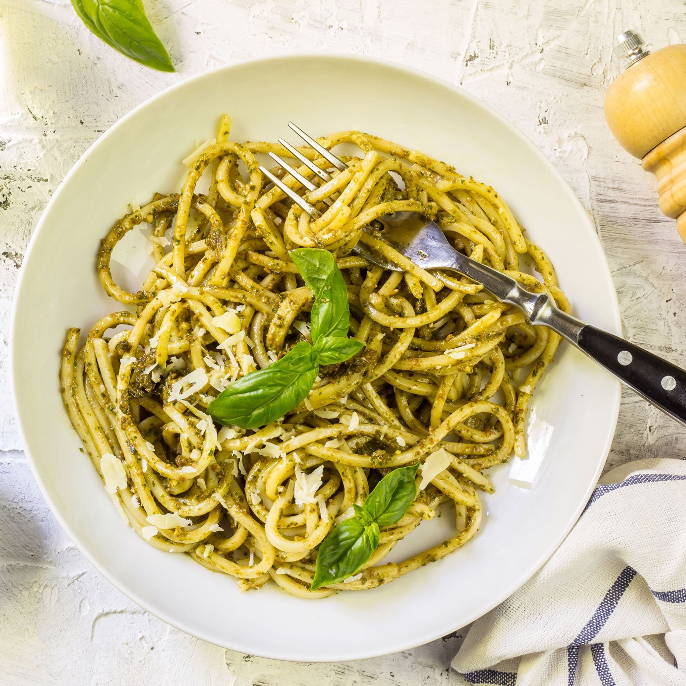 PIATTO DI LINGUINE AL PESTO IN PIATTO BIANCO SU PIANO DI CEMENTO BIANCO