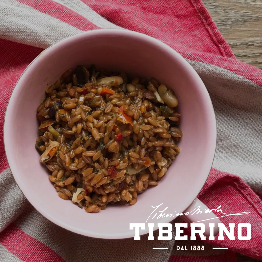 Zuppa di farro e lenticchie rosse in ciotola rosa su tovagliolo a righe rosse e bianche.