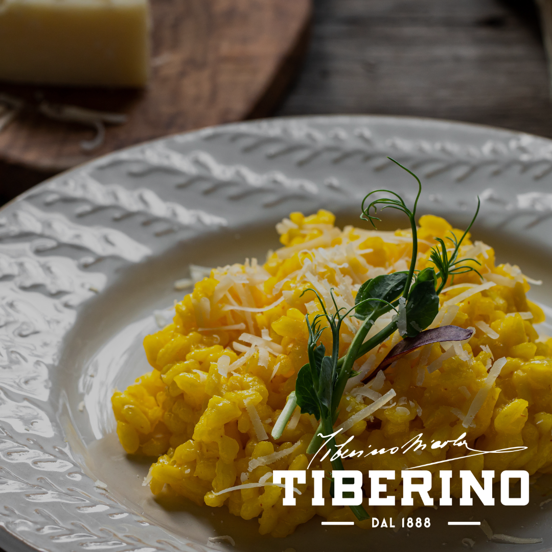 Risotto alla Milanese giallo dorato con parmigiano grattugiato e germogli verdi su piatto bianco decorato.