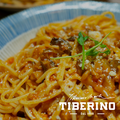 Spaghetti con sugo rosso ai funghi porcini, parmigiano grattugiato e germogli verdi, serviti in una ciotola bianca e blu.