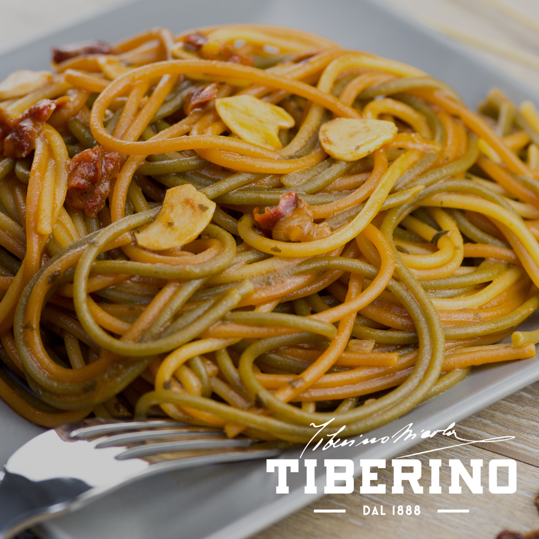 Spaghetti tricolori alle erbe aromatiche con aglio e pomodori secchi su piatto grigio.