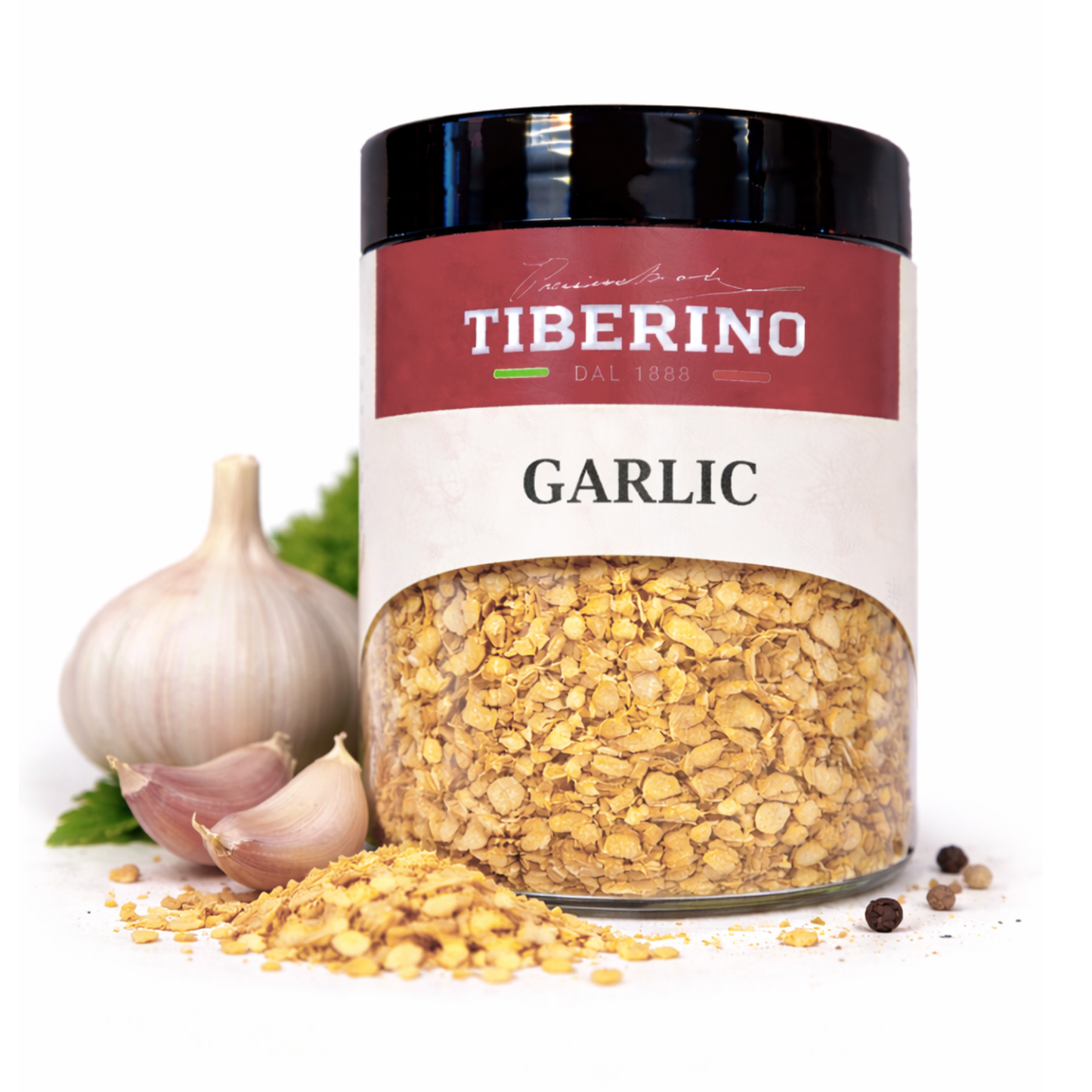 Barattolo di vetro trasparente Tiberino 1888 con aglio tostato essiccato in granuli dorati, aglio fresco e grani di pepe.