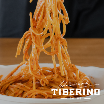 Bucatini all'Amatriciana con salsa rossa e guanciale, sollevati da un piatto bianco, logo Tiberino 1888.