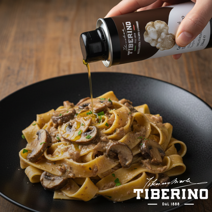 Mano versa olio al tartufo bianco Tiberino 1888 da lattina marrone da 250ml su pasta con funghi in piatto nero.