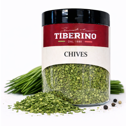 Barattolo trasparente Tiberino 1888 con erba cipollina essiccata, etichetta rossa e bianca, accanto a erba cipollina fresca e grani di pepe.