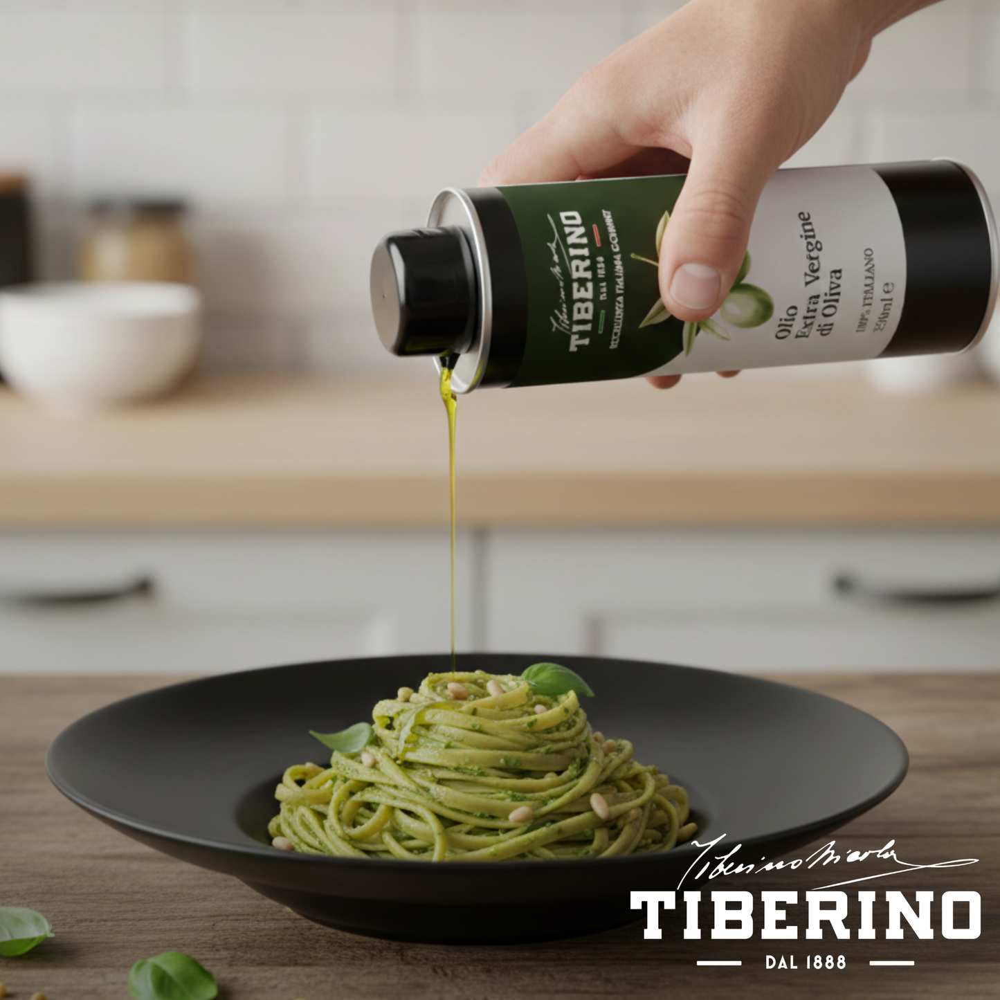 Mano versa olio extravergine Tiberino 1888 da lattina verde scuro su pasta al pesto con pinoli in piatto nero.