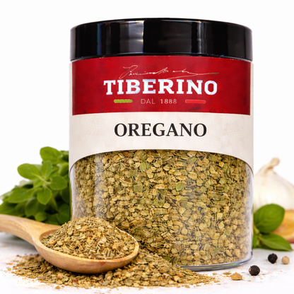 Barattolo trasparente di origano essiccato Tiberino 1888 con etichetta rossa, cucchiaio di legno e aglio.