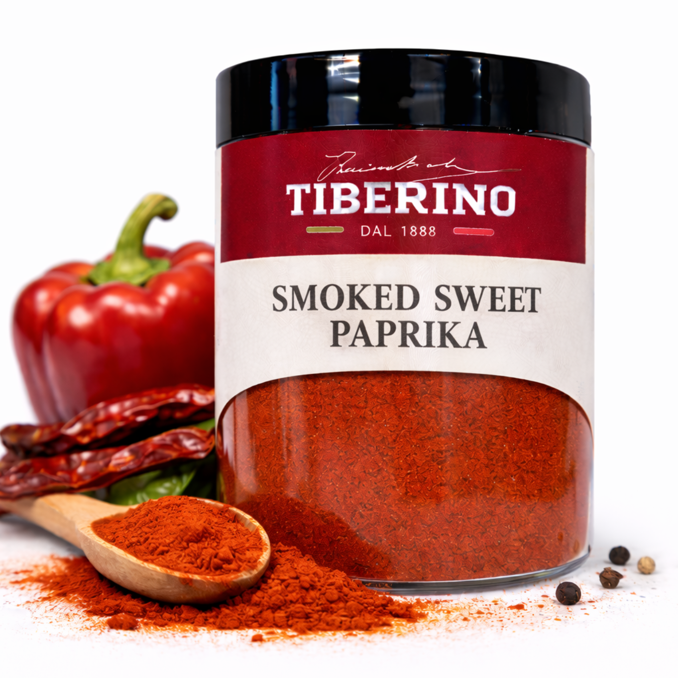 Vasetto trasparente di Paprika Dolce Affumicata Tiberino 1888 da 50g con etichetta rossa, cucchiaio di legno con paprika, peperone rosso e grani di pepe.