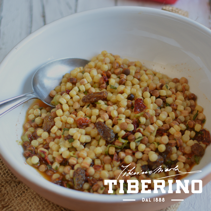 Pasta Fregola Sarda ai peperoni rossi e capperi al sale in una ciotola bianca con cucchiaio d'argento.