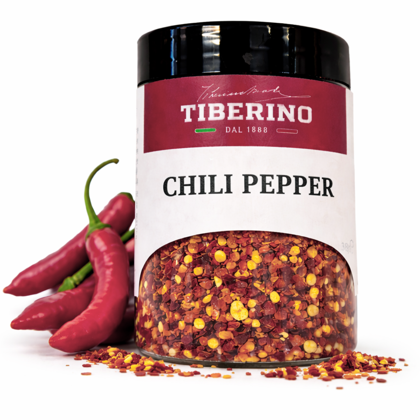 Vasetto trasparente Tiberino 1888 con peperoncino frantumato rosso e giallo, accanto a peperoncini freschi rossi.