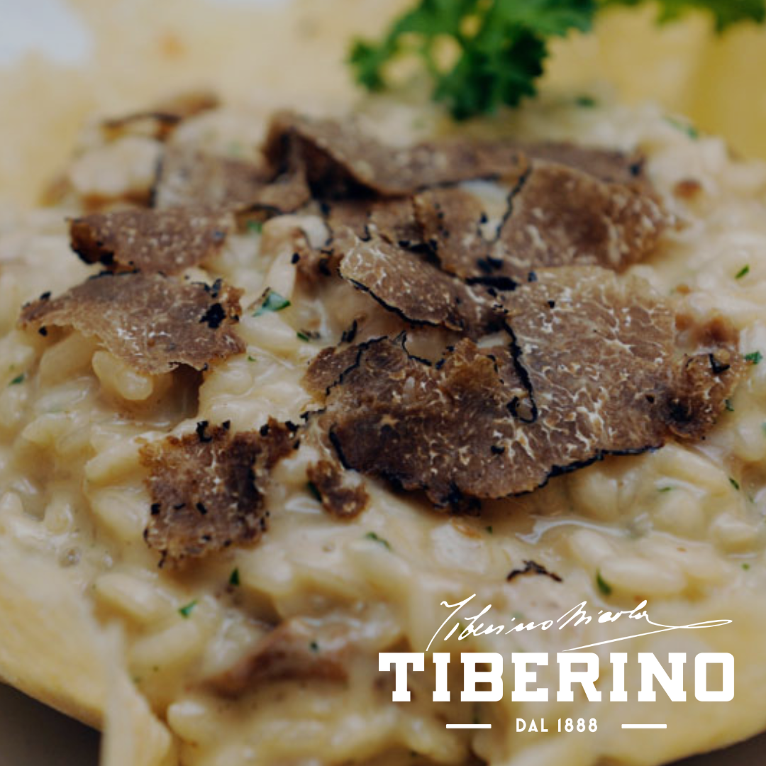 Risotto cremoso con scaglie di tartufo nero e prezzemolo fresco, servito in un piatto bianco.