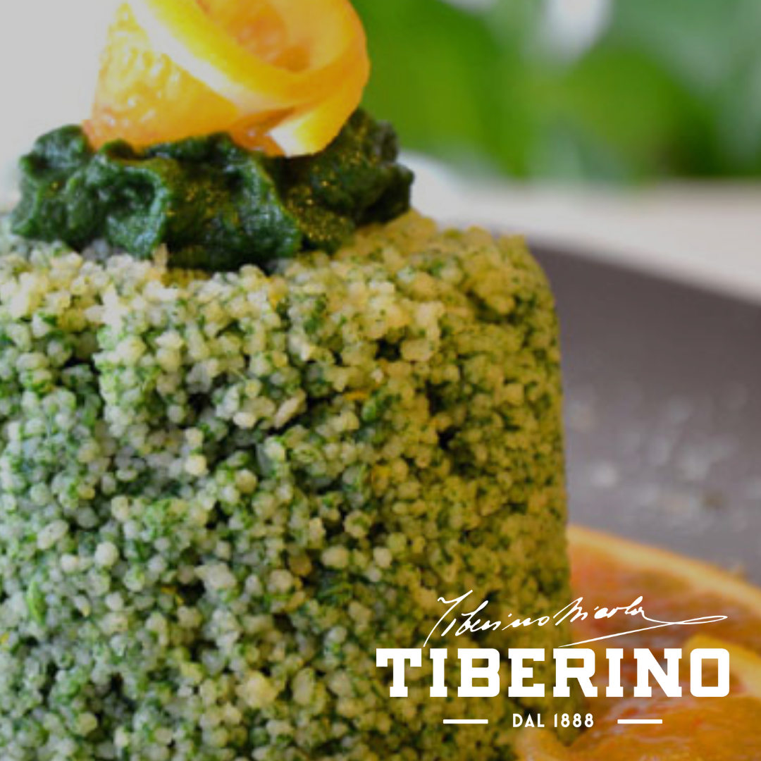 Risotto "Toscana" con spinaci, verde chiaro e scuro, guarnito con scorza d'arancia su piatto grigio.
