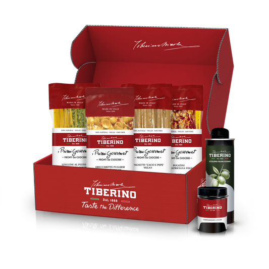 Scatola regalo rossa aperta di Tiberino 1888 con quattro confezioni di pasta vegana, una bottiglia di olio d'oliva e un vasetto.