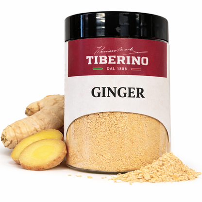 Barattolo di vetro trasparente con etichetta rossa e bianca "TIBERINO DAL 1888 GINGER", contenente zenzero in polvere giallo chiaro, accanto a radici di zenzero fresco e fette.