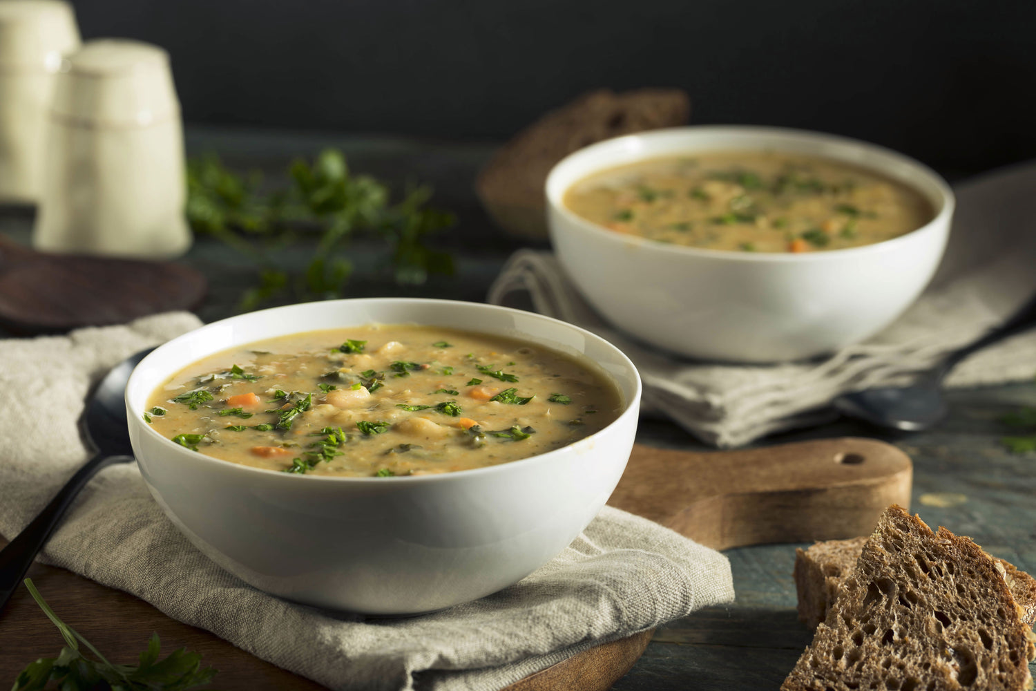 Due ciotole bianche di zuppa di fagioli pugliese con carote, prezzemolo e pane integrale su tagliere di legno.