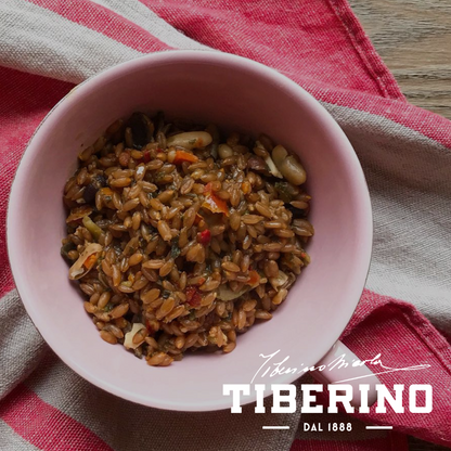 Zuppa di farro e lenticchie rosse in ciotola rosa su tovagliolo a righe rosse e bianche.